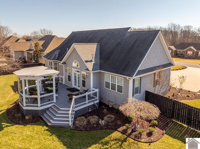 rear view of house with a lawn, roof with shingles, a deck, and fence