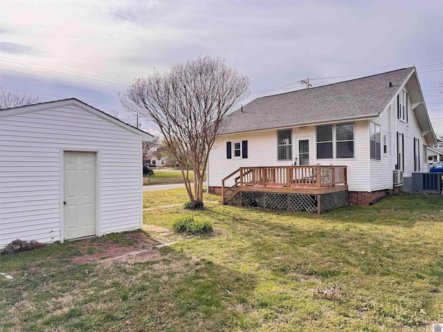 back of property featuring a lawn, a deck, cooling unit, an outdoor structure, and a shingled roof