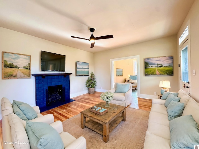 living room featuring baseboards, a fireplace, a ceiling fan, and light wood-style floors