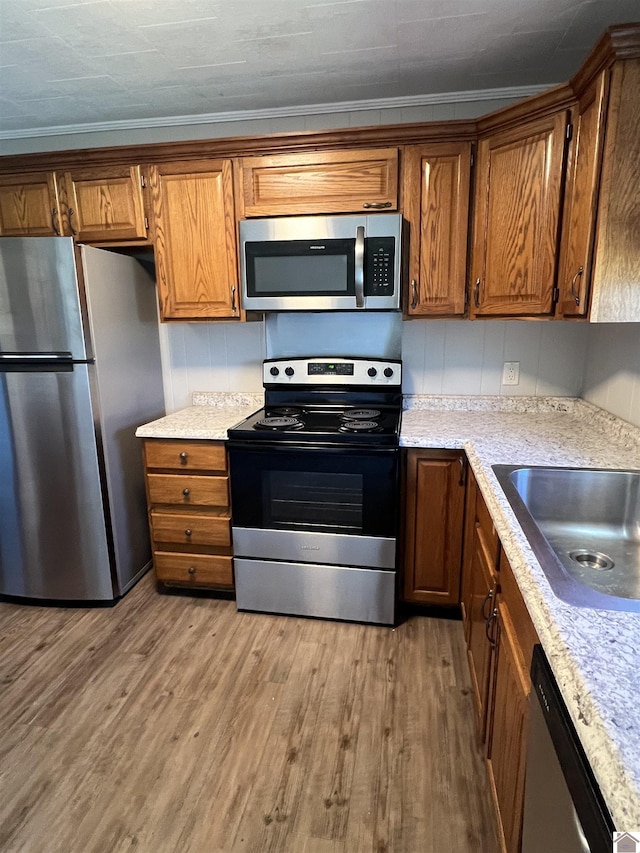 kitchen with a sink, stainless steel appliances, brown cabinets, and light wood finished floors