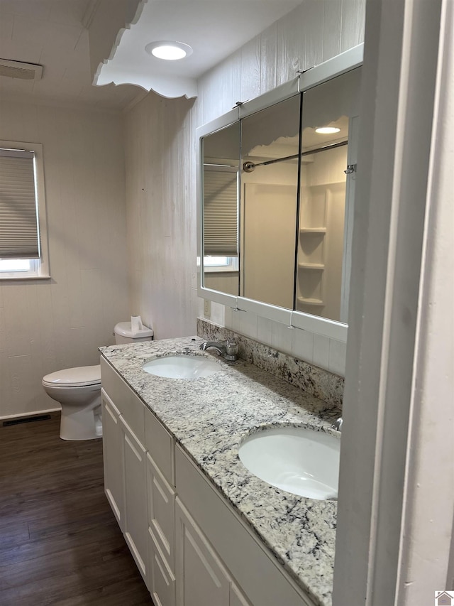 bathroom featuring toilet, wood finished floors, double vanity, and a sink