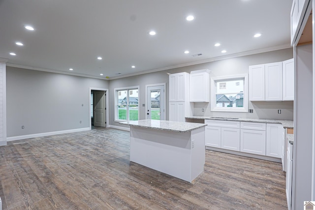 kitchen with a center island, crown molding, light stone counters, and white cabinets