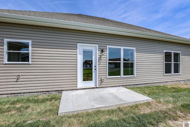 doorway to property featuring roof with shingles, a yard, and a patio