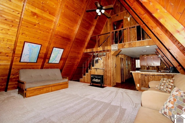 carpeted living room featuring lofted ceiling with beams, stairway, wood walls, ceiling fan, and wooden ceiling