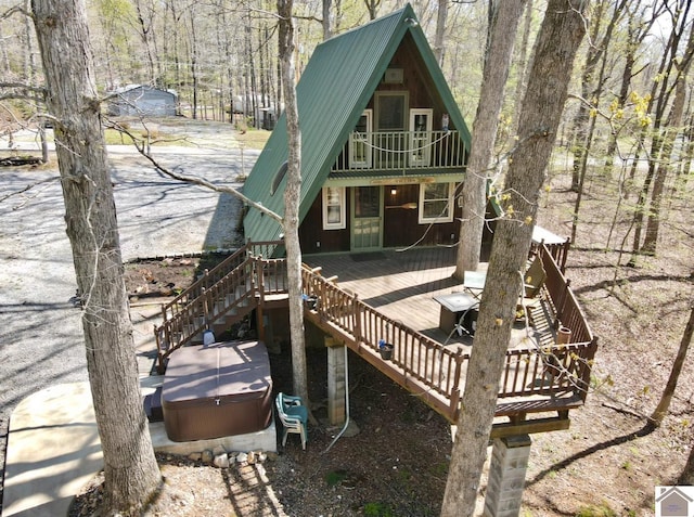 back of house featuring a jacuzzi, metal roof, a view of trees, a balcony, and stairs