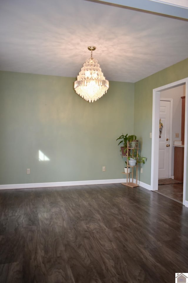 empty room with a chandelier, baseboards, and dark wood finished floors