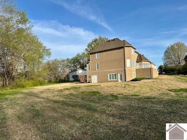 back of house with stucco siding and a lawn