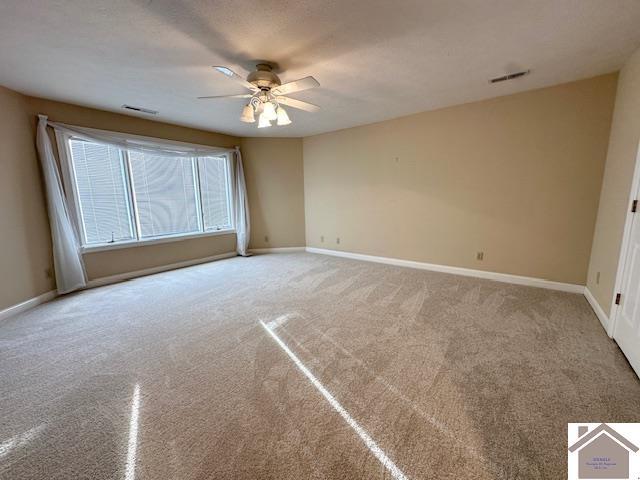 carpeted spare room featuring visible vents, baseboards, and ceiling fan