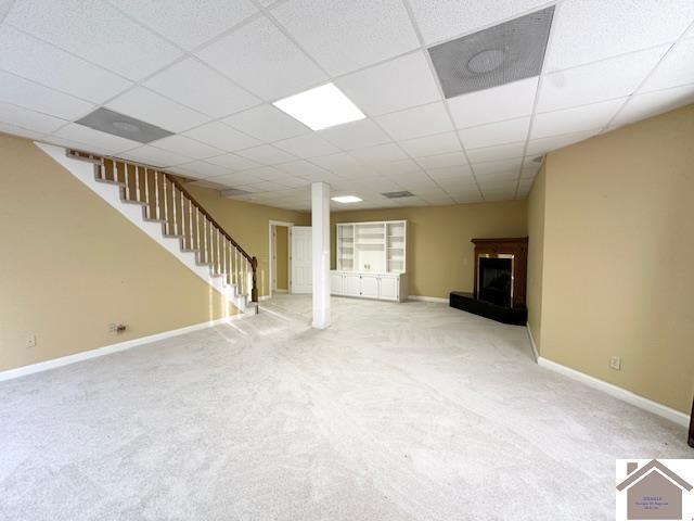 unfurnished living room featuring baseboards, a fireplace with raised hearth, carpet, and stairs