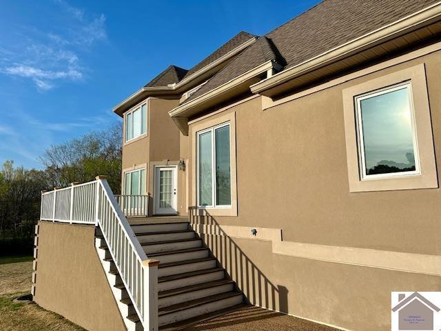 view of home's exterior featuring a shingled roof, stucco siding, and stairway