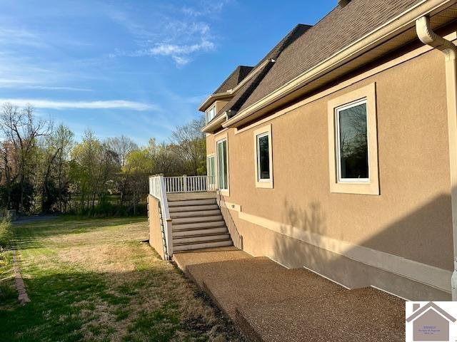 view of side of home with stairway, a deck, a lawn, and stucco siding