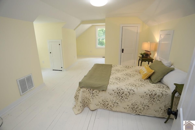 bedroom featuring visible vents, light wood-type flooring, and vaulted ceiling