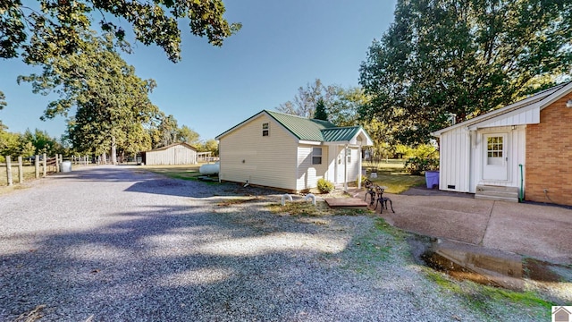 view of property exterior featuring an outdoor structure, gravel driveway, entry steps, metal roof, and fence