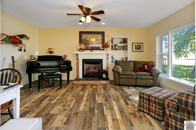 living area with wood finished floors, ceiling fan, a fireplace with raised hearth, and plenty of natural light
