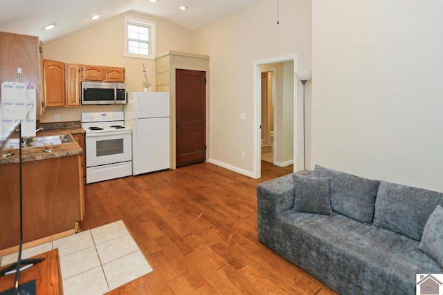 kitchen featuring baseboards, a sink, white appliances, wood finished floors, and high vaulted ceiling