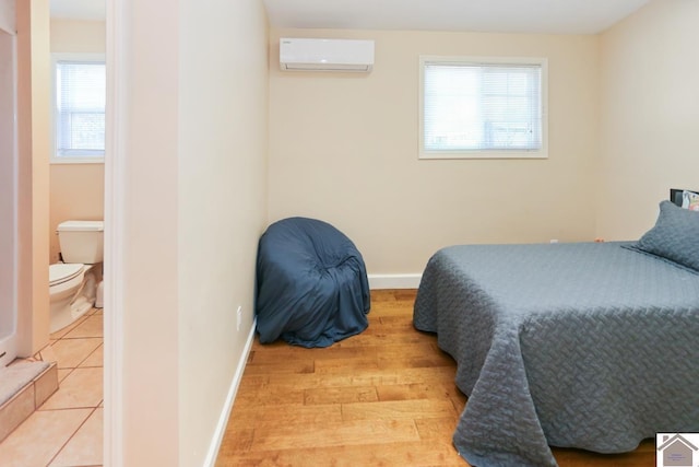 bedroom featuring multiple windows, an AC wall unit, baseboards, and light wood-style flooring