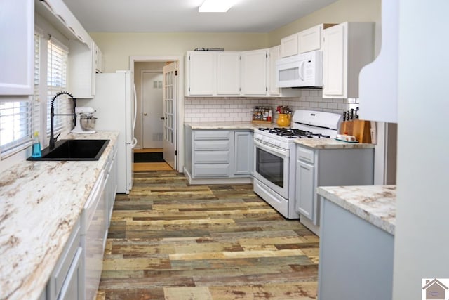 kitchen featuring wood finished floors, decorative backsplash, a sink, and white appliances