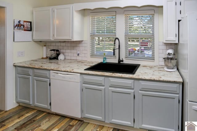kitchen with tasteful backsplash, wood finished floors, a sink, and white appliances