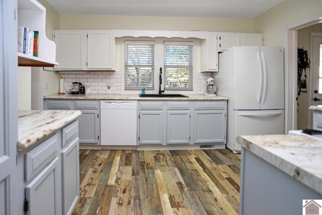 kitchen featuring white appliances, light stone countertops, tasteful backsplash, wood finished floors, and a sink