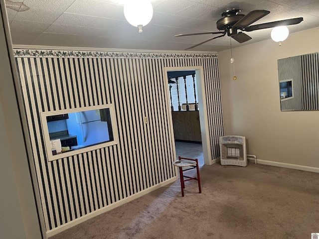 carpeted spare room featuring baseboards, a ceiling fan, and heating unit