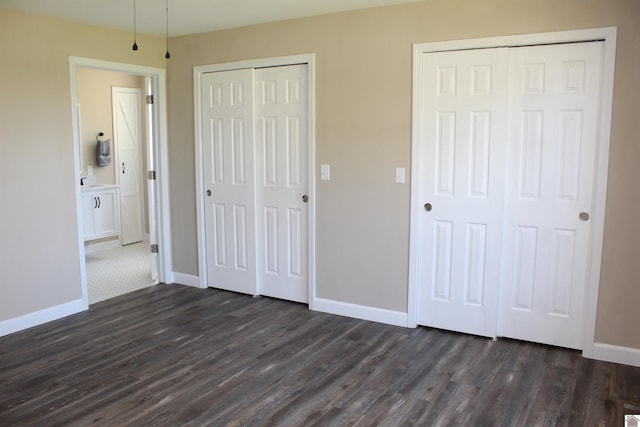 unfurnished bedroom with baseboards, multiple closets, and dark wood-style floors