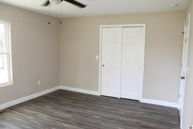 unfurnished bedroom featuring ceiling fan, baseboards, dark wood-style floors, and a closet