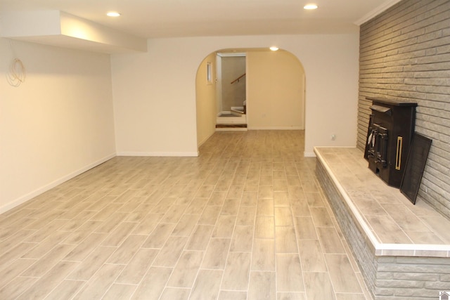 unfurnished living room featuring recessed lighting, stairway, arched walkways, baseboards, and a brick fireplace