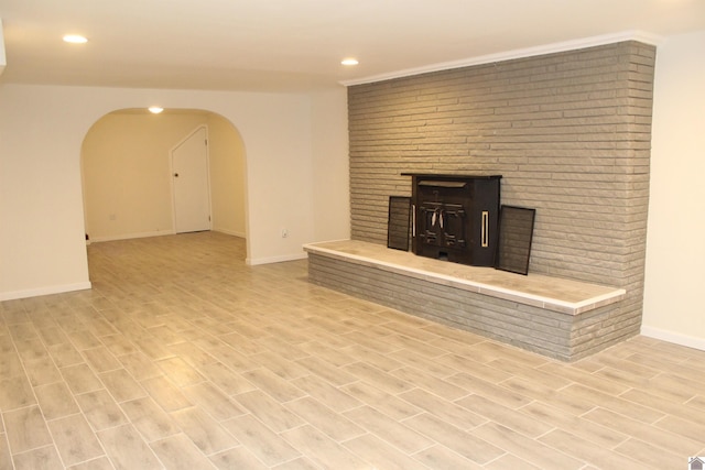 unfurnished living room featuring light wood-style flooring, arched walkways, baseboards, recessed lighting, and a brick fireplace