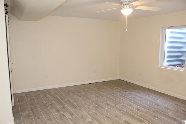unfurnished room featuring a barn door, baseboards, a ceiling fan, and wood finished floors