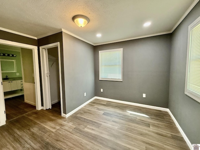 unfurnished bedroom with a sink, baseboards, recessed lighting, wood finished floors, and crown molding