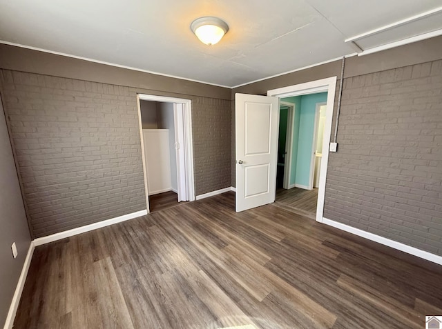 unfurnished bedroom featuring brick wall, wood finished floors, baseboards, and a closet