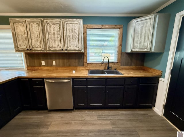 kitchen with stainless steel dishwasher, a sink, light wood-style floors, light countertops, and ornamental molding