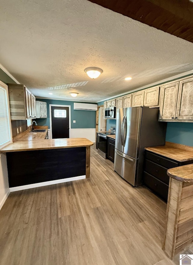 kitchen featuring a peninsula, a wall mounted AC, light wood-style floors, and appliances with stainless steel finishes
