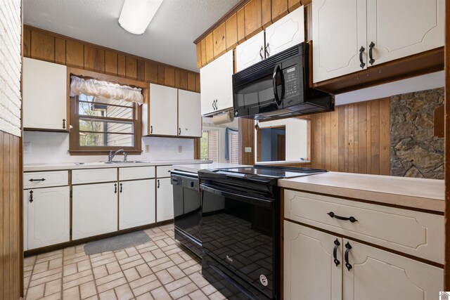 kitchen featuring black appliances, wood walls, a sink, and light countertops