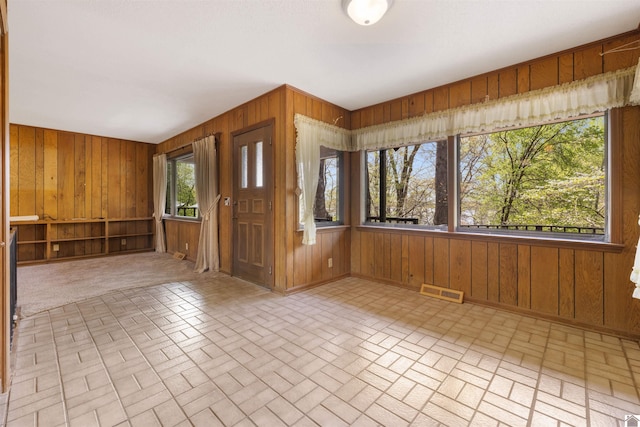 unfurnished room featuring brick patterned floor, wooden walls, visible vents, and baseboards