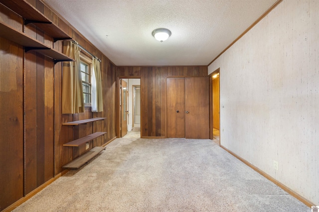 unfurnished bedroom featuring a textured ceiling, baseboards, light colored carpet, wood walls, and a closet