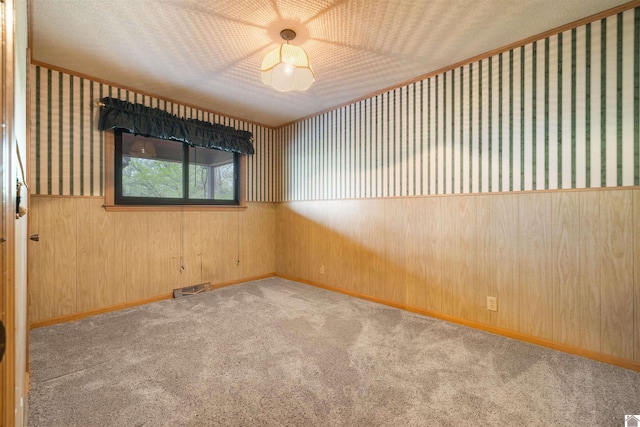 carpeted spare room with wallpapered walls, a wainscoted wall, visible vents, and a textured ceiling
