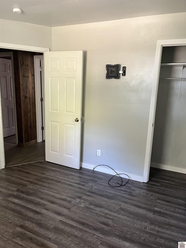 unfurnished bedroom with baseboards, dark wood-style floors, and a closet