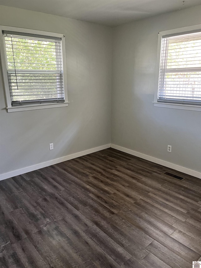 spare room featuring dark wood finished floors, a healthy amount of sunlight, and visible vents