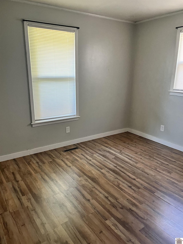 spare room featuring visible vents, baseboards, wood finished floors, and ornamental molding