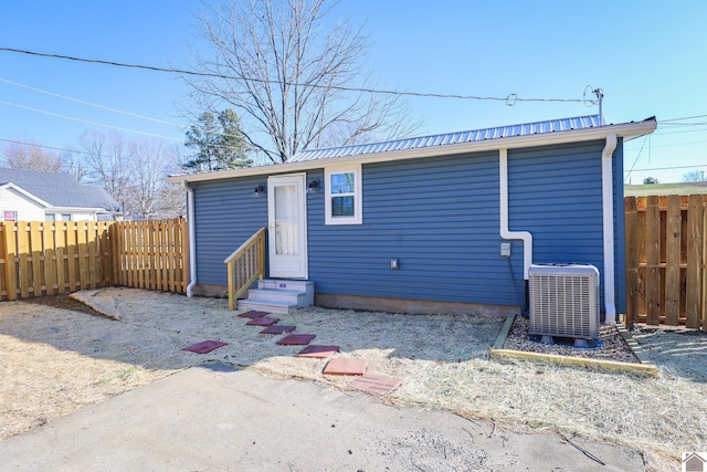 rear view of property with entry steps, central AC unit, a fenced backyard, and metal roof