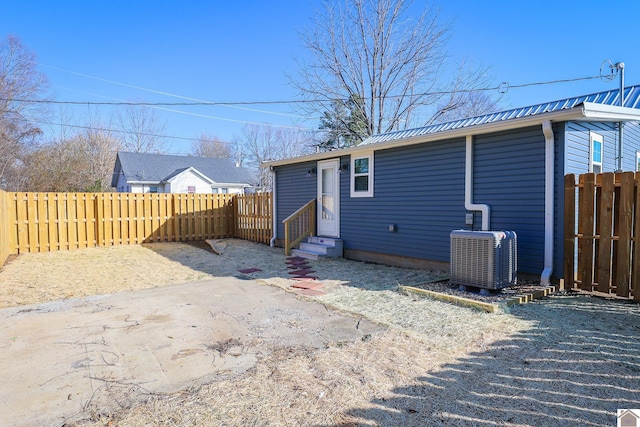 rear view of property with metal roof, central AC, entry steps, and a fenced backyard