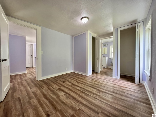 unfurnished bedroom with a textured ceiling, wood finished floors, and baseboards