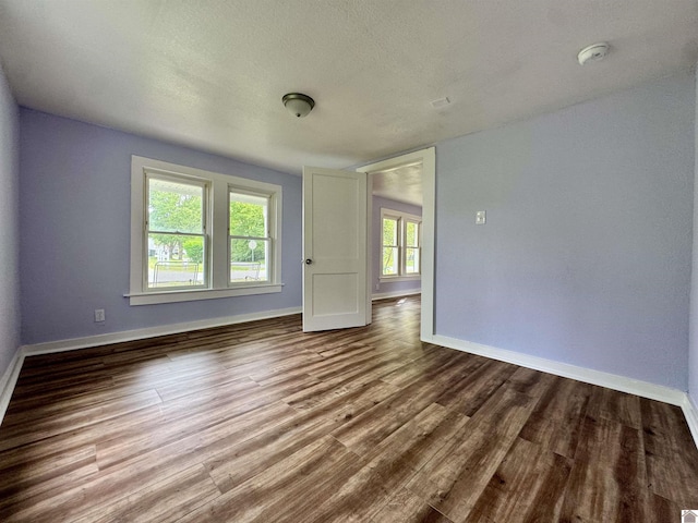 spare room with a textured ceiling, wood finished floors, and baseboards