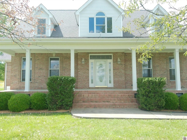 exterior space featuring a shingled roof, covered porch, and brick siding