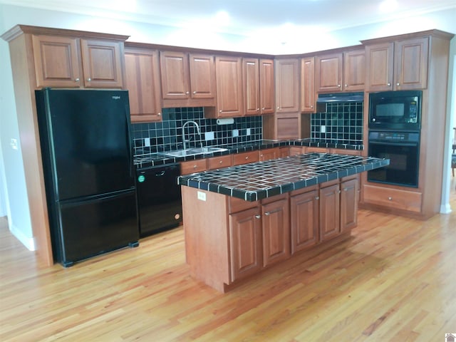 kitchen featuring decorative backsplash, a sink, tile counters, black appliances, and light wood-type flooring