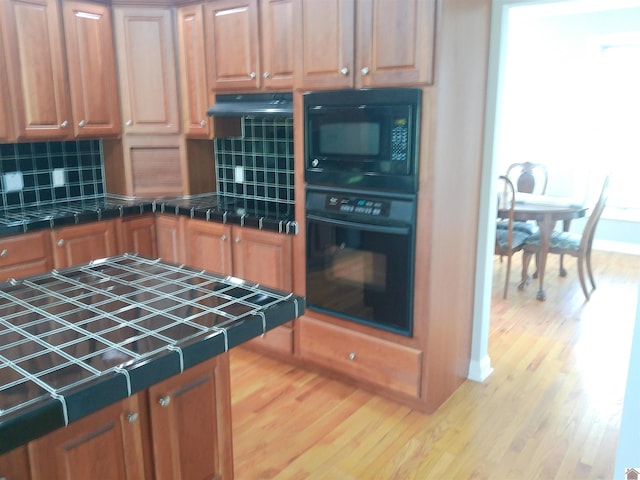 kitchen with tasteful backsplash, tile counters, baseboards, black appliances, and wood finished floors