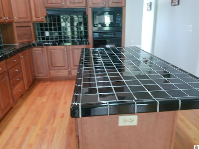 kitchen with black appliances, tile counters, light wood-style flooring, and under cabinet range hood