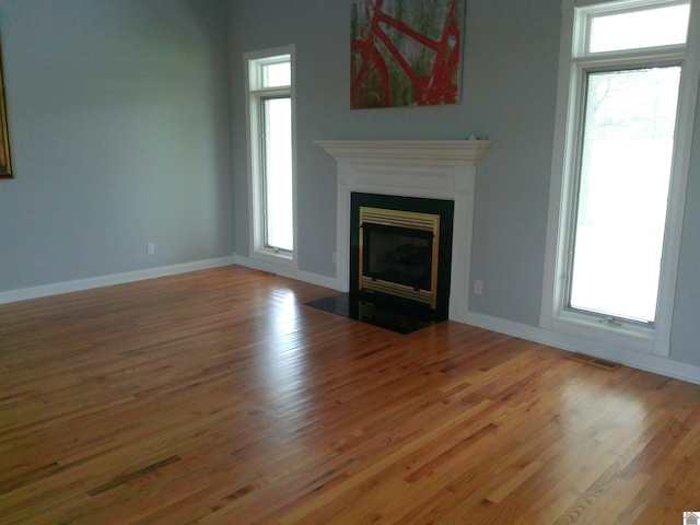 unfurnished living room with baseboards, visible vents, wood finished floors, and a fireplace with flush hearth