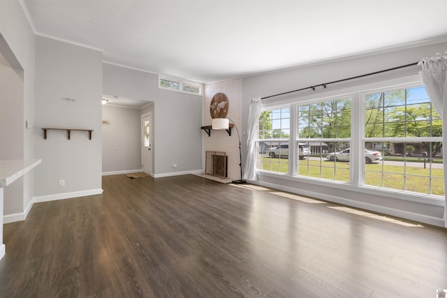 unfurnished living room featuring baseboards, wood finished floors, crown molding, and a brick fireplace